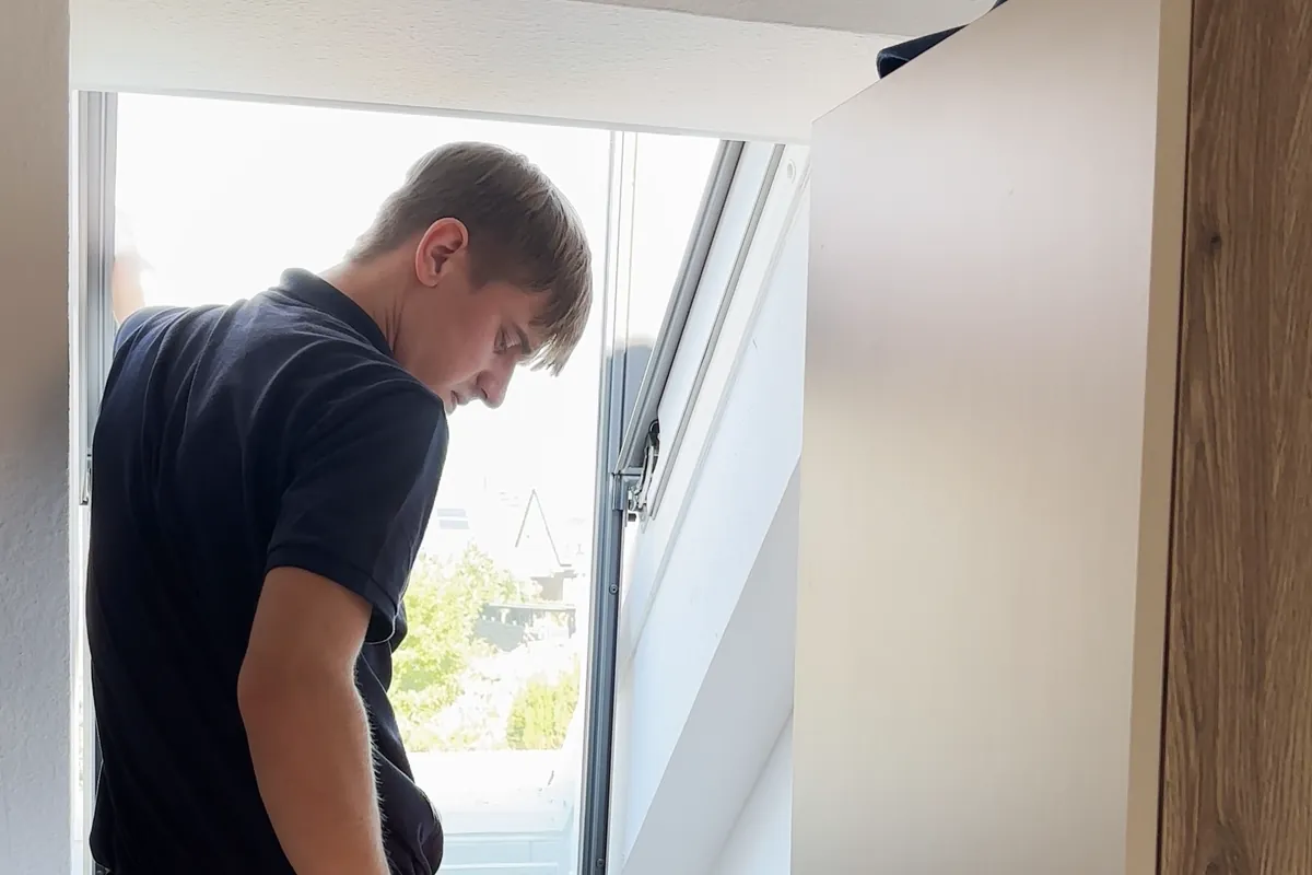 Ein GE+ES-Mitarbeiter reinigt ein Dachfenster von der Leiter aus